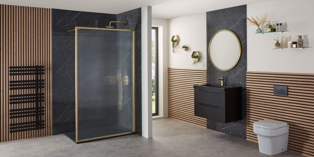 Modern bathroom with black and wood panelled walls, gold-framed glass shower, round mirror, black vanity unit, wall-mounted toilet, towel rail, and shelves with decor and toiletries. Large window provides natural light.